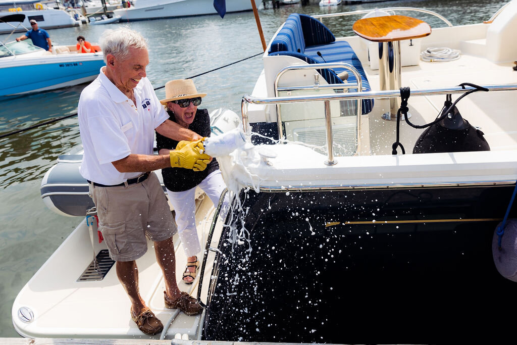 Someone excitedly smashes champagne on the side of a boat.