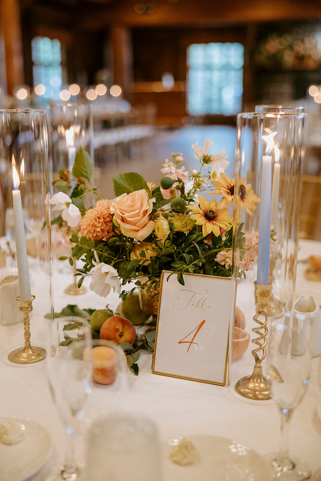Gold compote vase with peach roses and dahlias, rudbeckia, fruit and candles on table in Great Hall in Sunriver