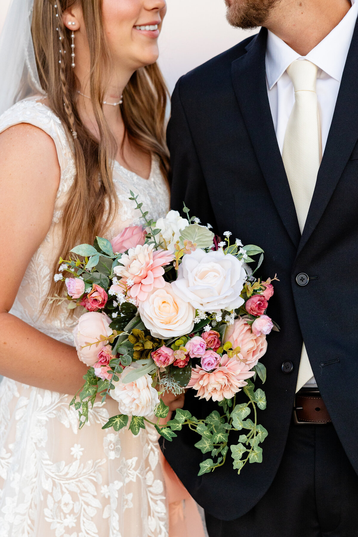 Bride and groom share a joyful moment, holding a bouquet of pastel roses and greenery.
