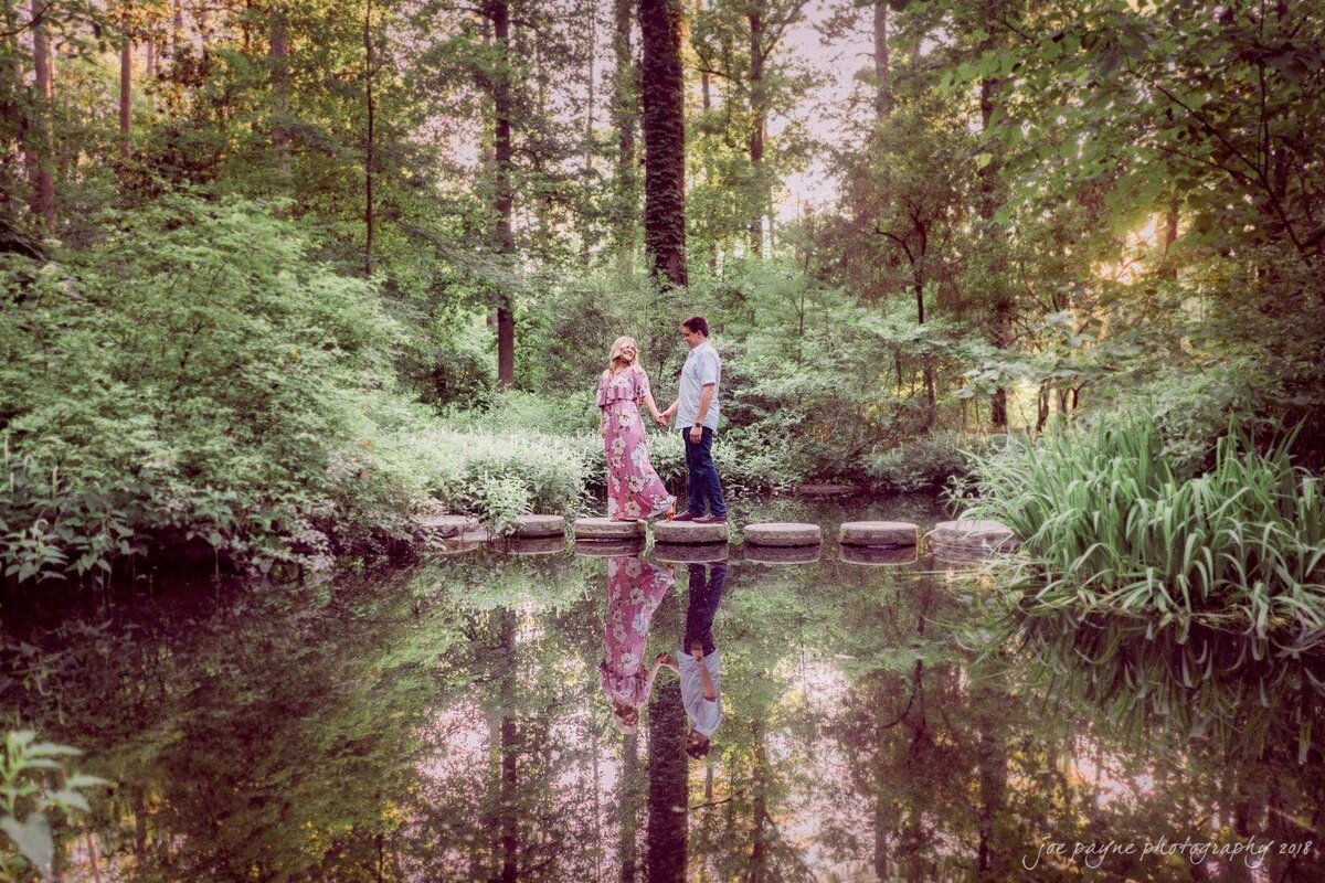 A couple holding hands and walking on stones over a river.