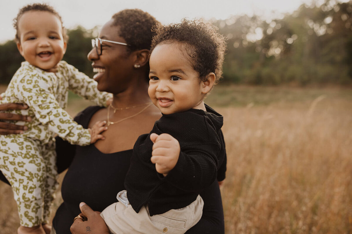 Joyful mother holds her twin baby boys, one on each hip, in Minnesota meadow