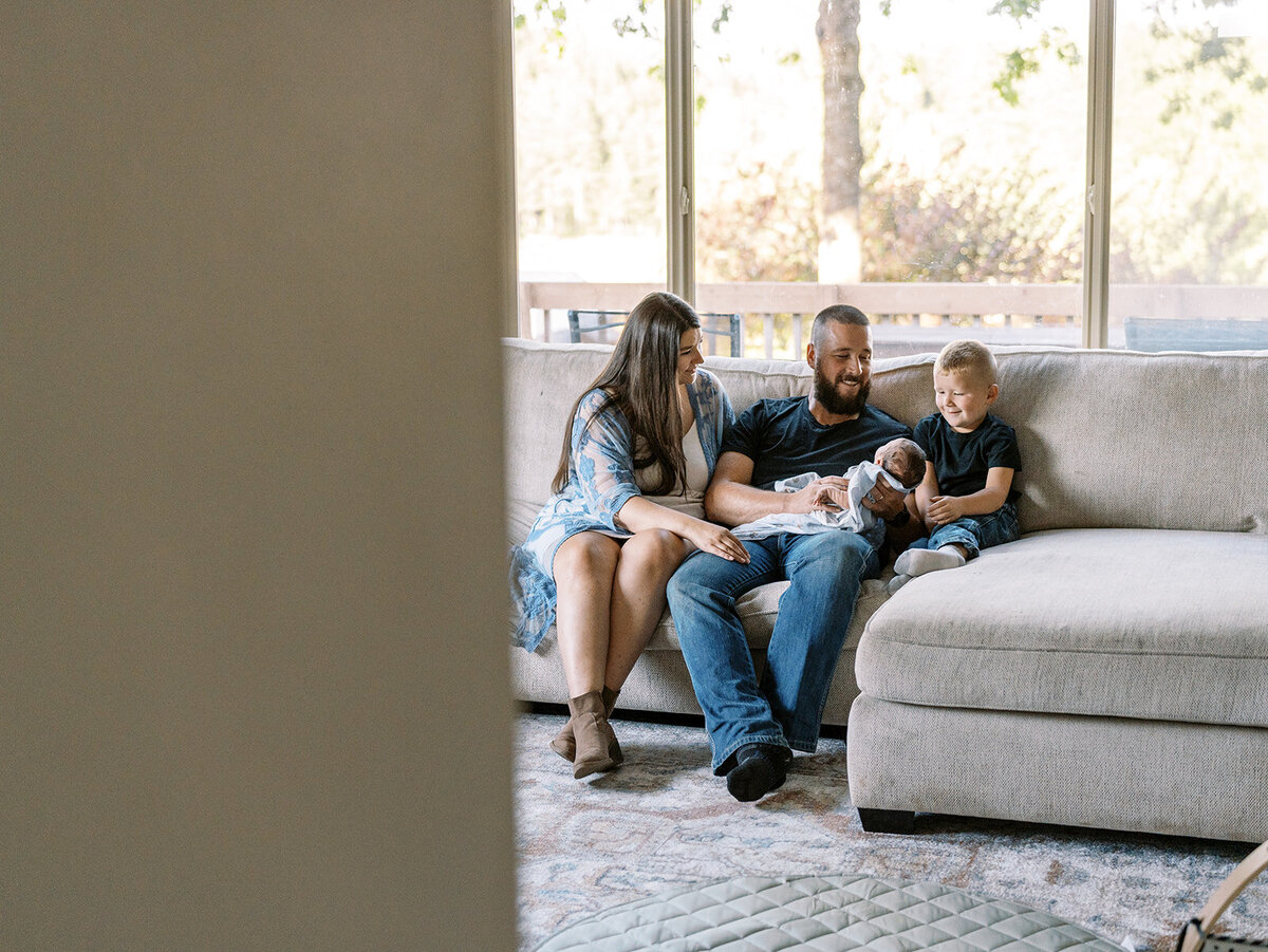 A family sitting on a couch smiling at a baby.
