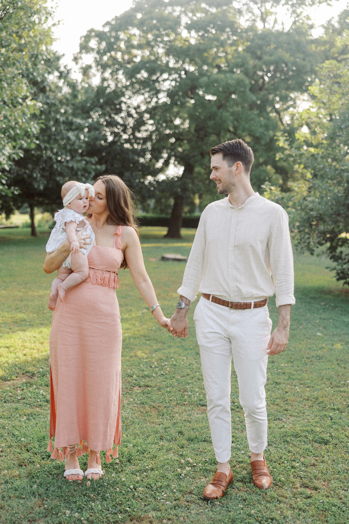stylish young couple hold hands while mom carries baby girl at woodward park