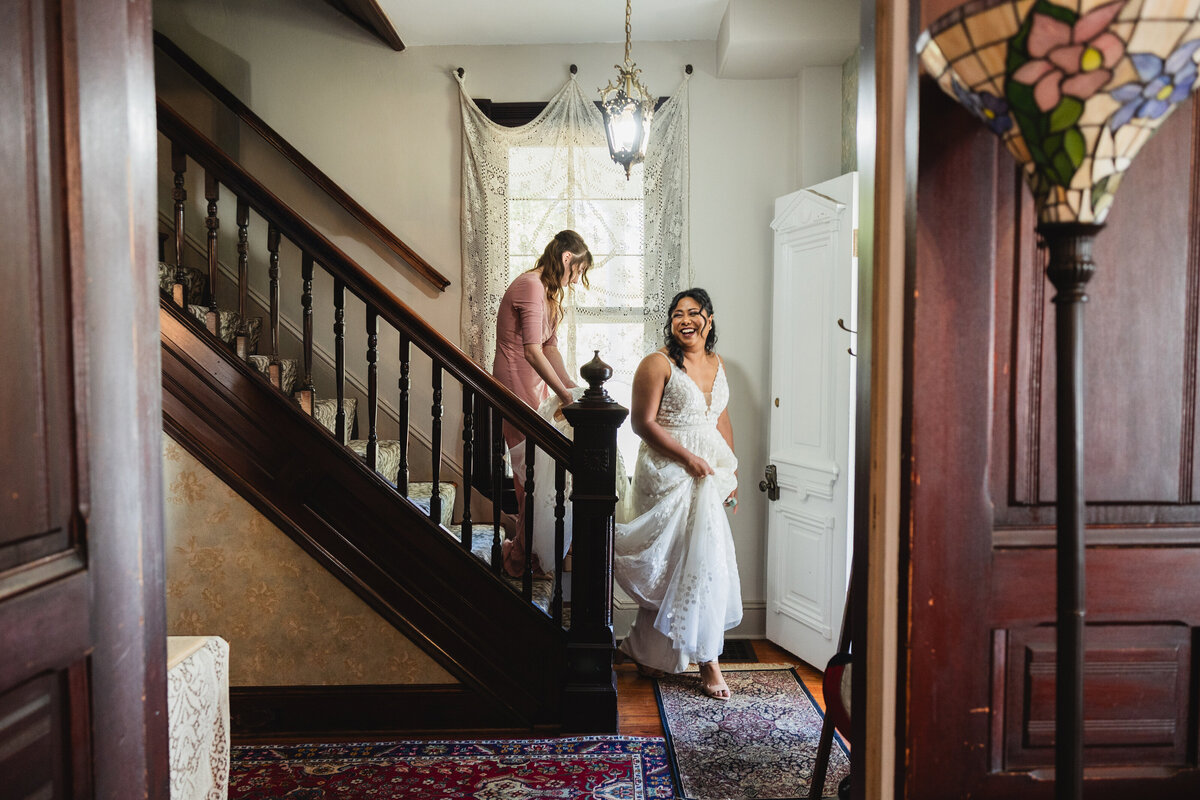 A person in a wedding dress walking down the stairs while someone holds their train behind them