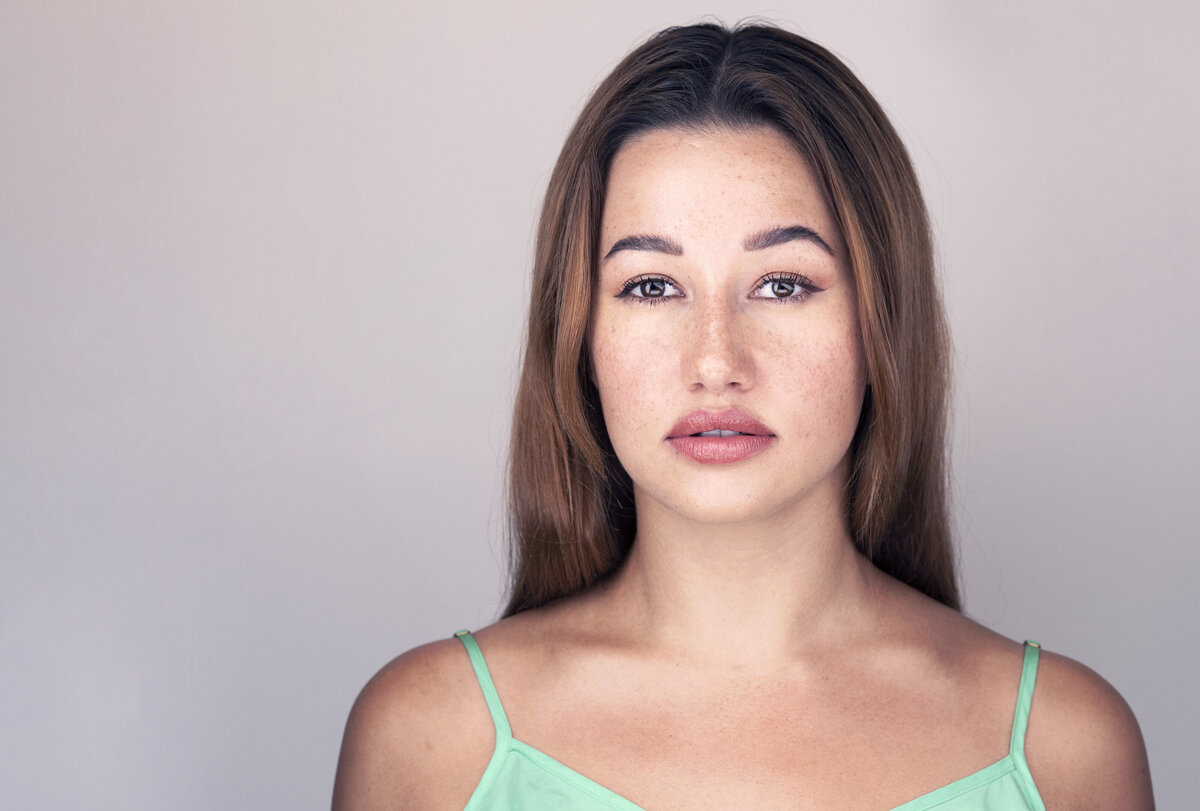 Woman in green tank top is posing for a studio headshot. Her long brown hair is pushed behind her shoulders. She is looking at the camera with her lips slightly apart. Captured by Liza Nicole Photography | Philadelphia and Main Line Headshot Photographer.