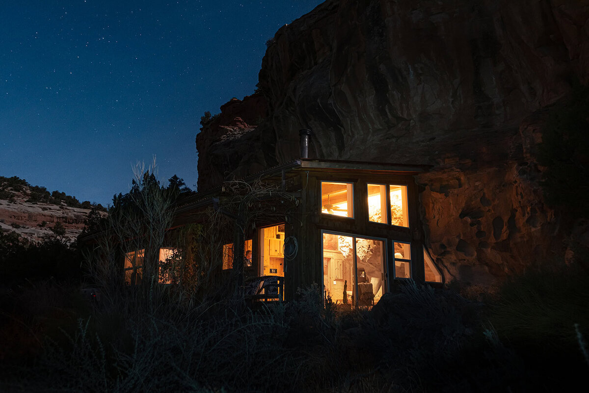 An adventure luxe cabin connected to a sandstone cliff glows with warm light in the darkness of the night in the image capture by a photographer specializing in luxury elopements.