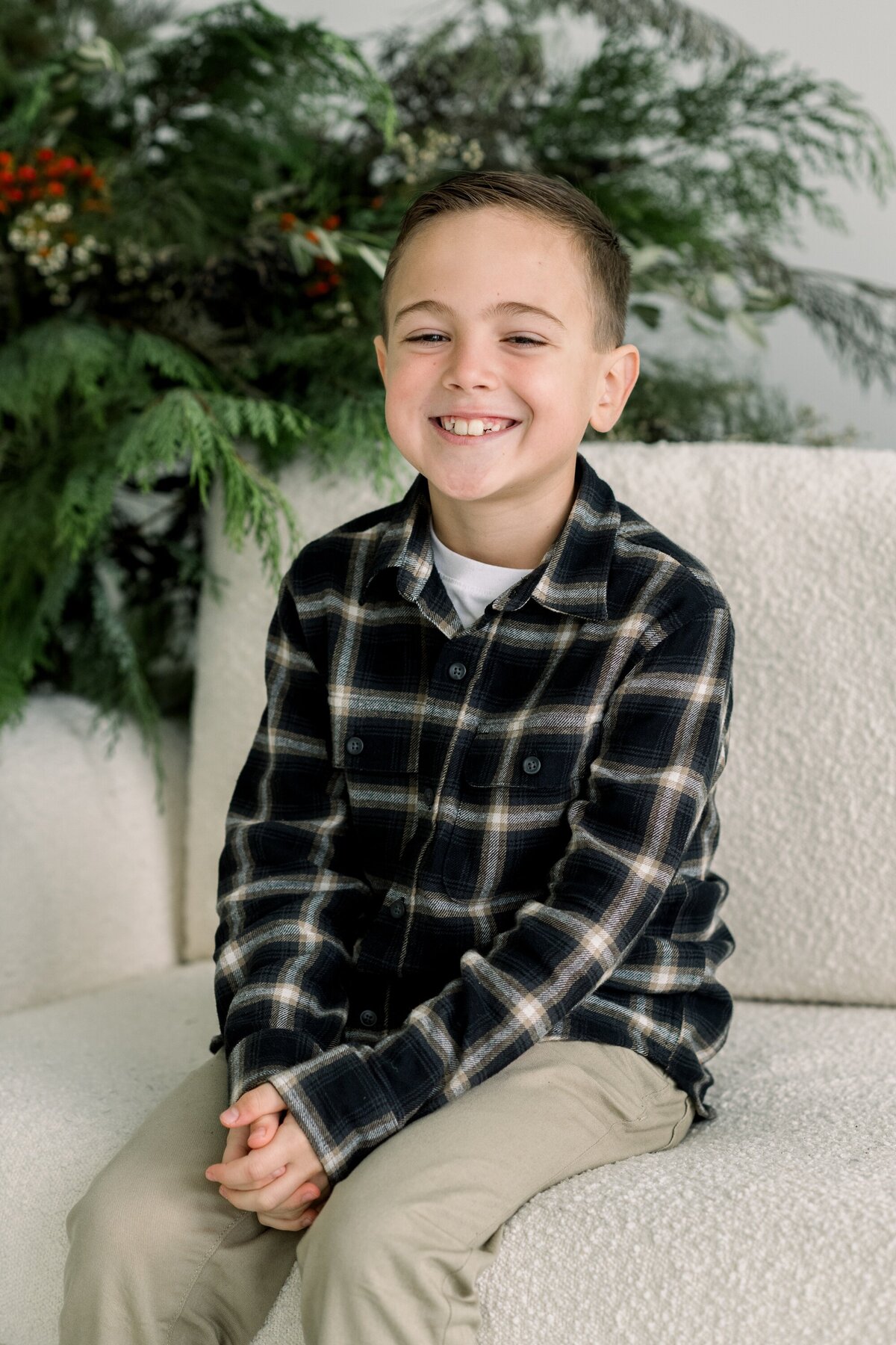 Young boy in black and white flannel on white couch.