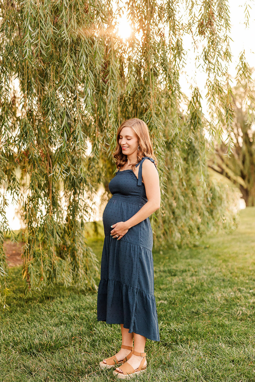 Pregnant woman smiling next to a willow tree