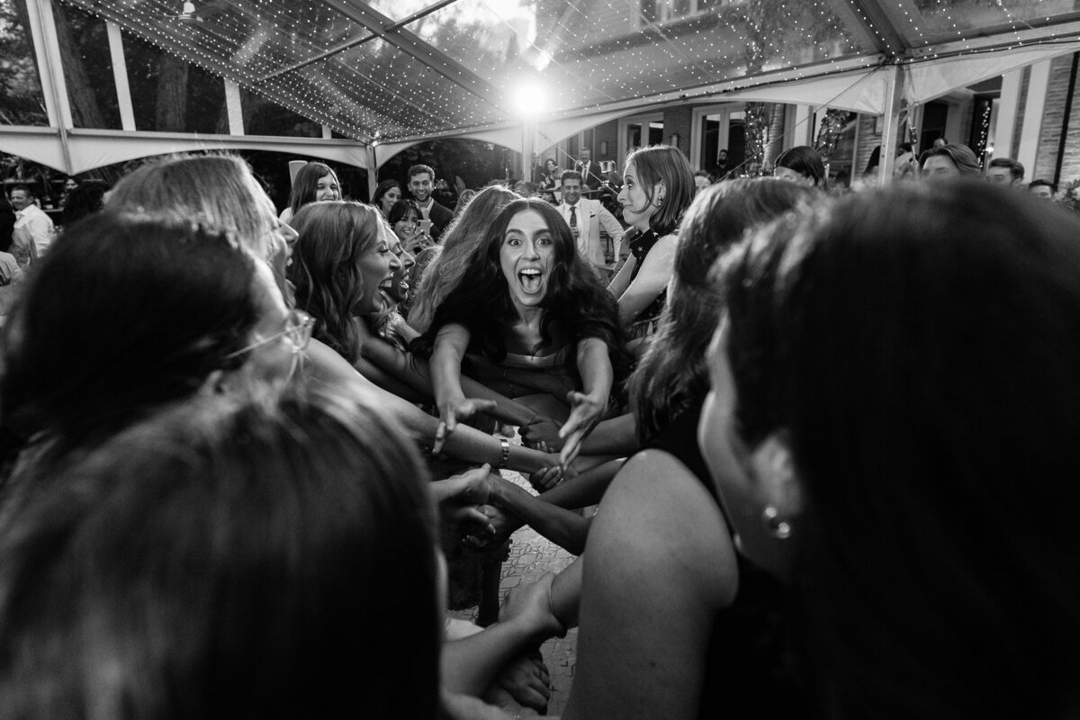Fun bride being thrown in the air during a hora in black and white