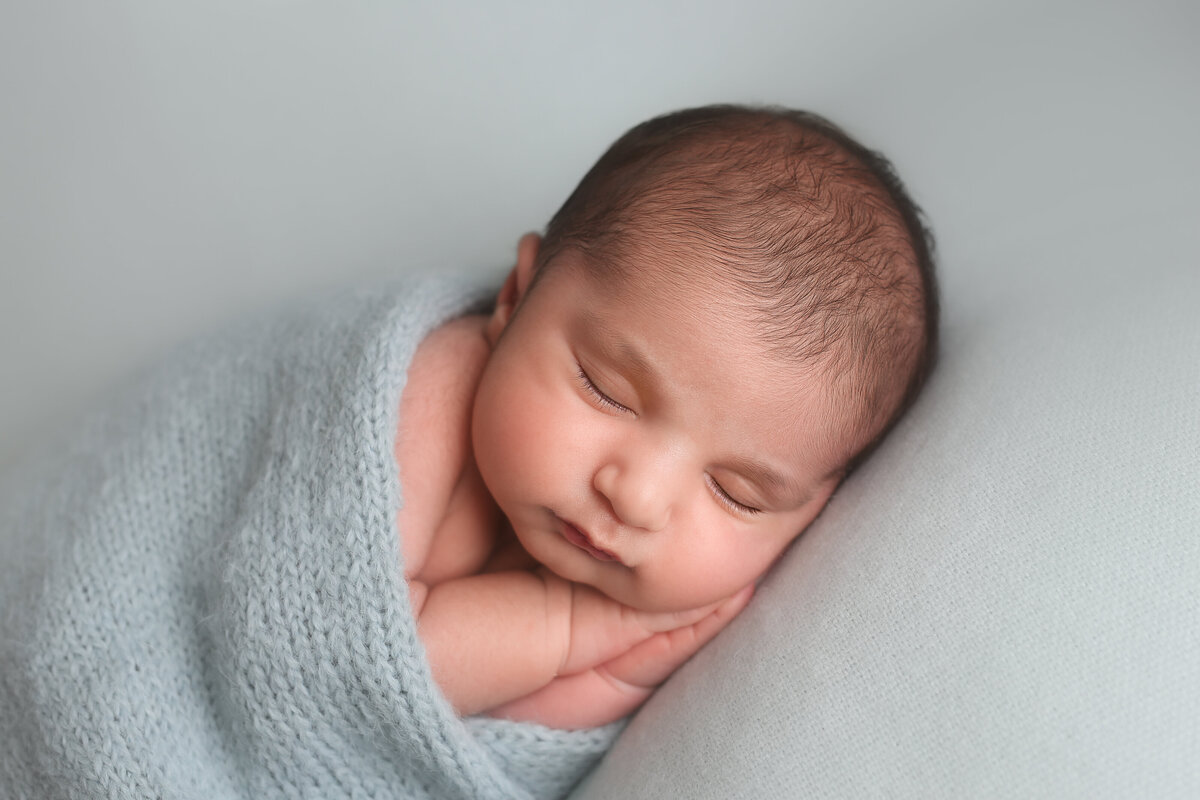 Newborn boy wrapped in blue wrap & lying on his side