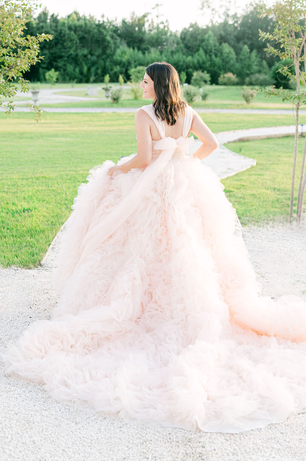 A bride in a voluminous blush gown walks gracefully along a garden path at her Savannah wedding, radiating elegance and romance. Amia Marcell savannah wedding and editorial Photographer.