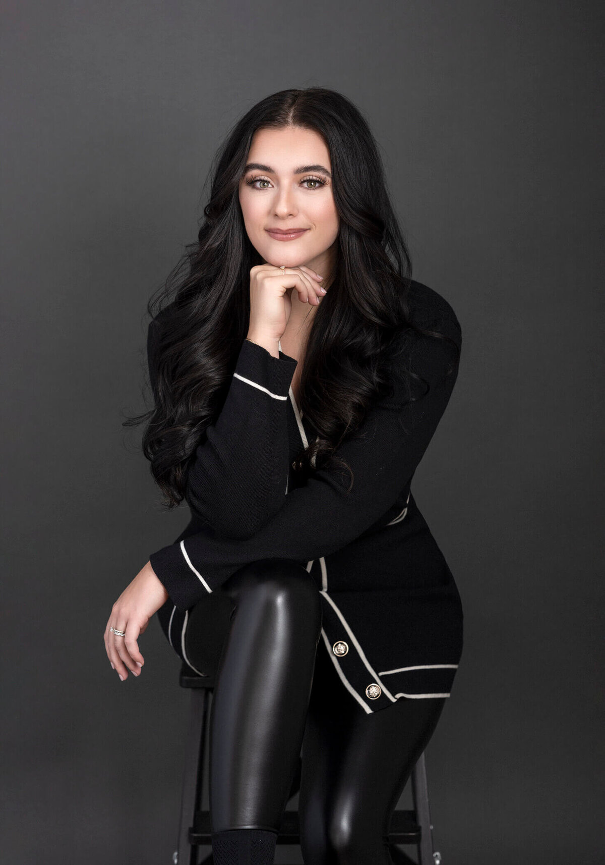 Young woman with long black hair, wearing a black outfit, resting her chin on her hand.