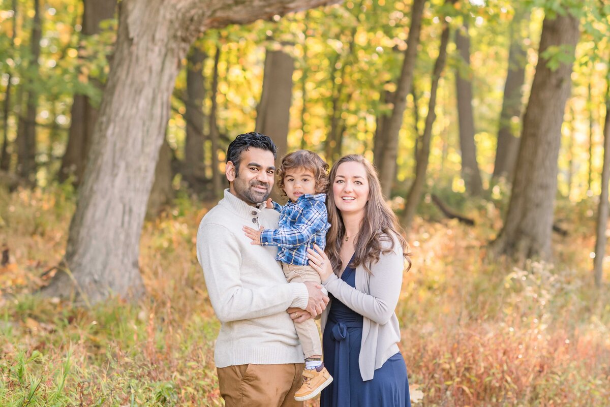 Oak Park IL family photos in the fall woods; a mom and dad hugging their toddler son