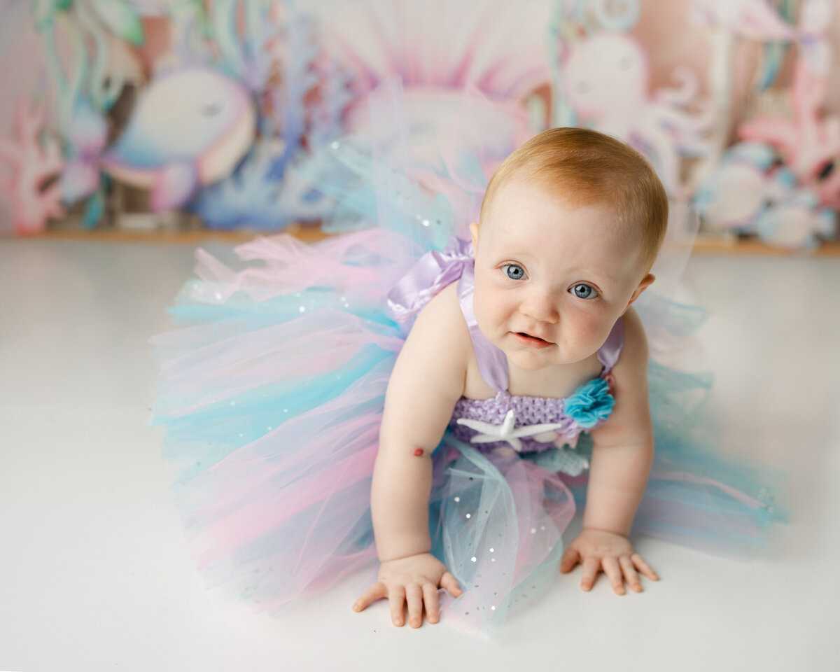 Baby crawling in a pastel mermaid tutu with an ocean-themed backdrop. Photograph by Yucaipa cake smash photographer Kaitlyn Dawn Photography.