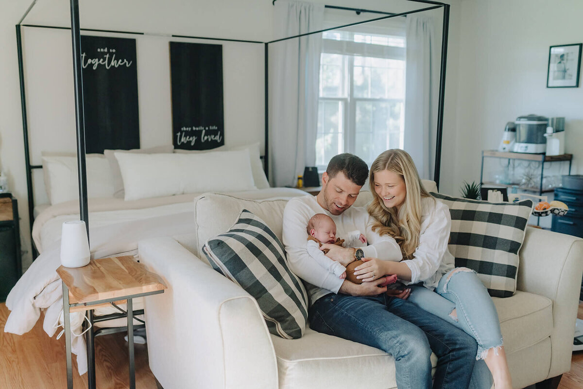 couple sitting on sofa looking at newborn baby for newborn photoshoot at Finger Lakes, NY