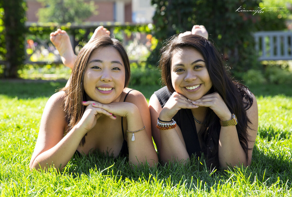 Two smiling girls posing with head in hands on the grass