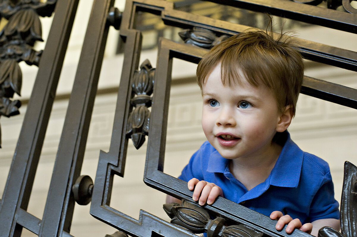 A small child smiling with their head through a square railing 