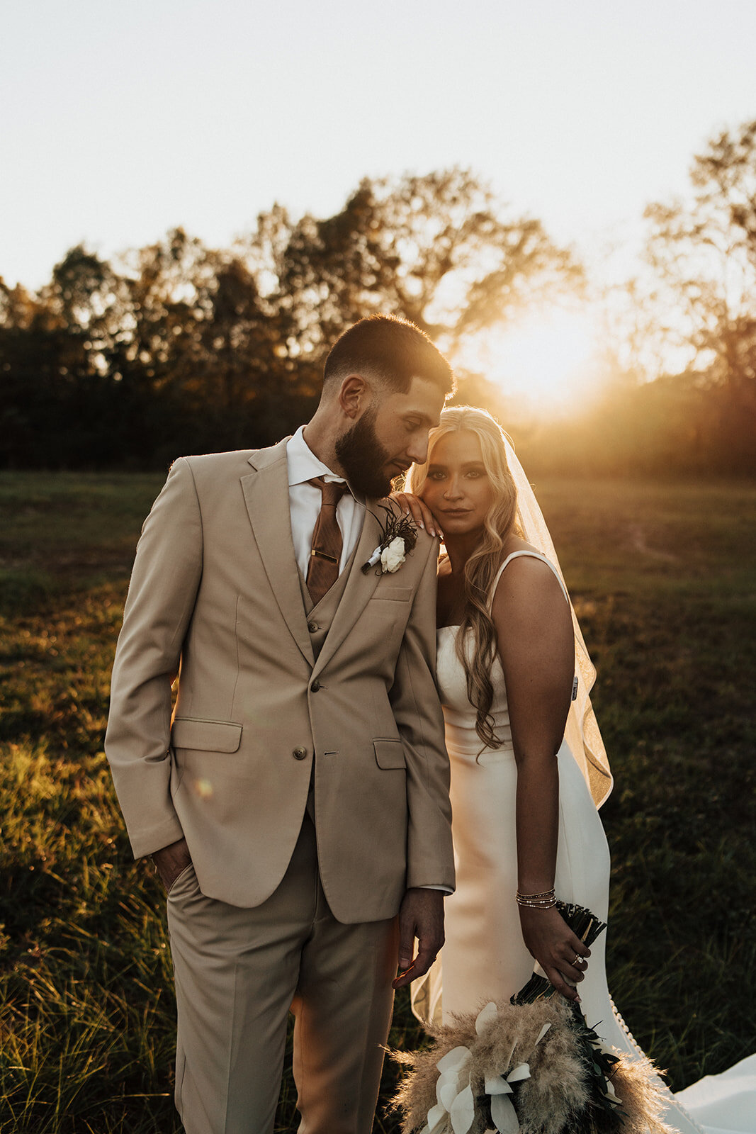Bride looking at the camera and groom staring at bride at sunset in an open field