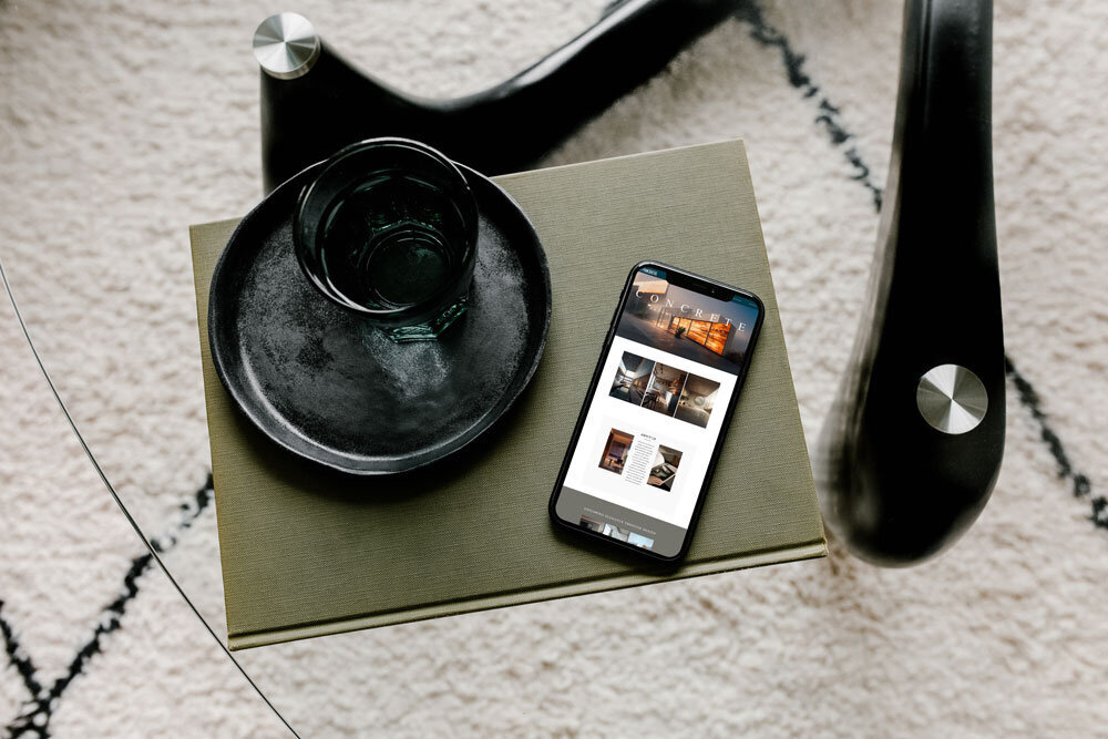 iPhone displaying the Concrete Architectural Design website resting on a green book, blending modern design with natural elements.