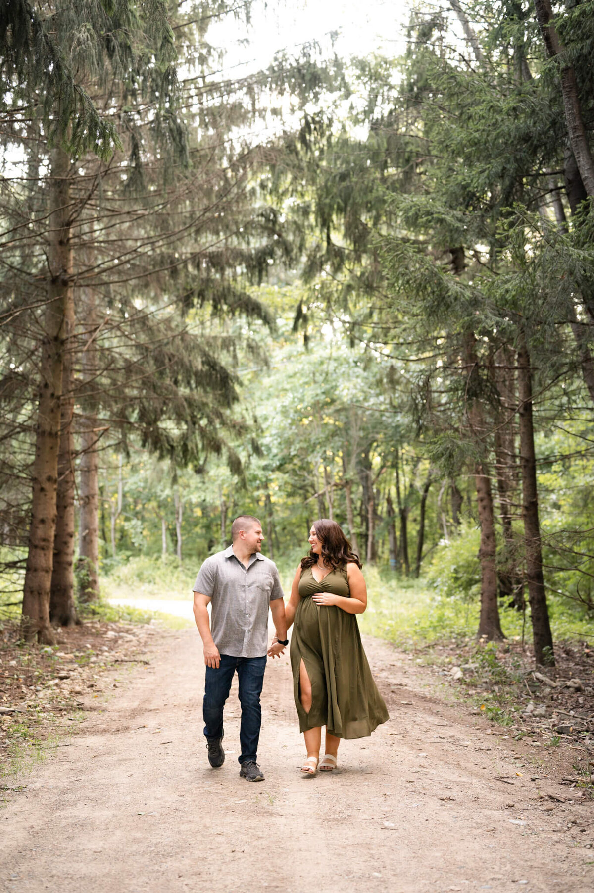 Couple walks through tall pine trees while posing for maternity photos