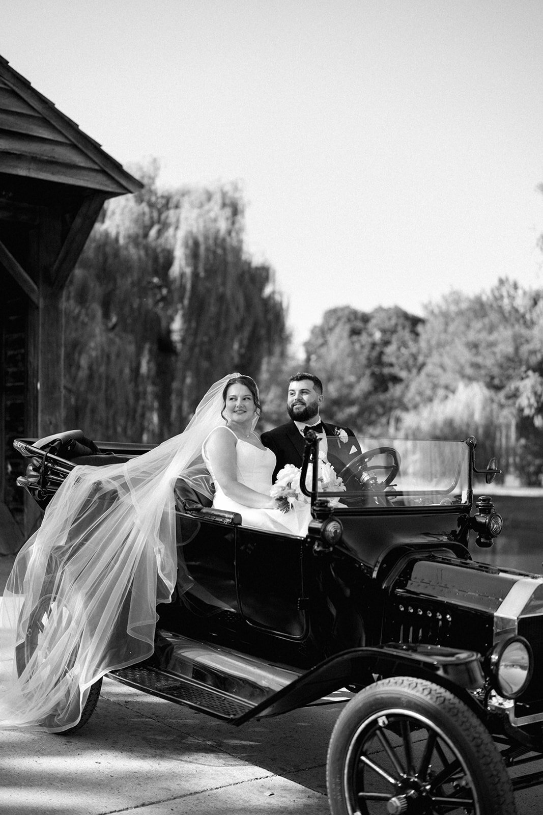 Bride and groom riding in a vintage car at Dearborn Village Michigan, classic wedding portrait with flowing veil.