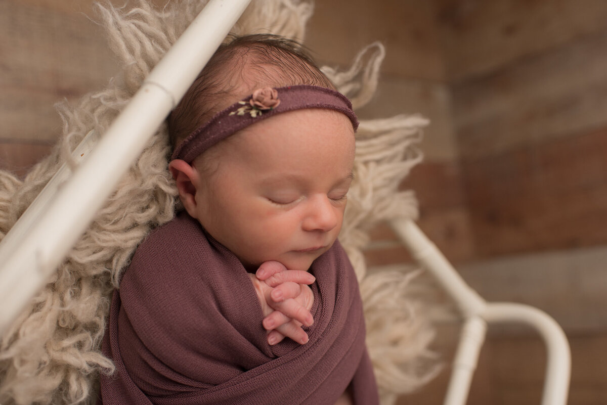 Baby girl wrapped in purple, white crib, purple headband, posed