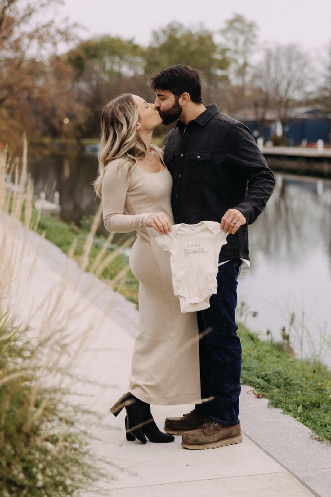 Man and woman holding baby onesie for baby announcement photos in Finger Lakes New York
