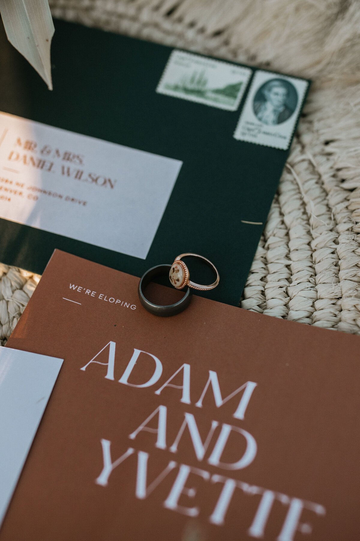 Black and rose gold wedding bands set atop mixed wedding stationery with white lettering on a table charger.