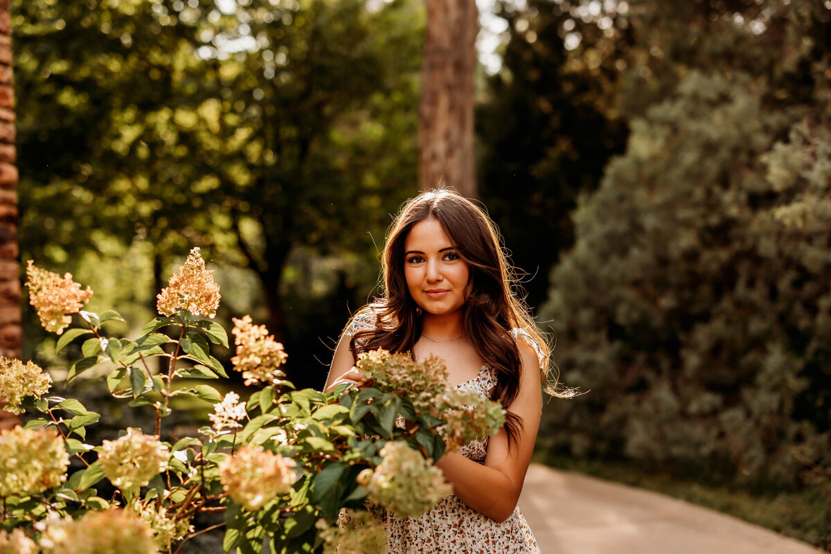 Teenage girl stands behind flowers during fall senior photo session