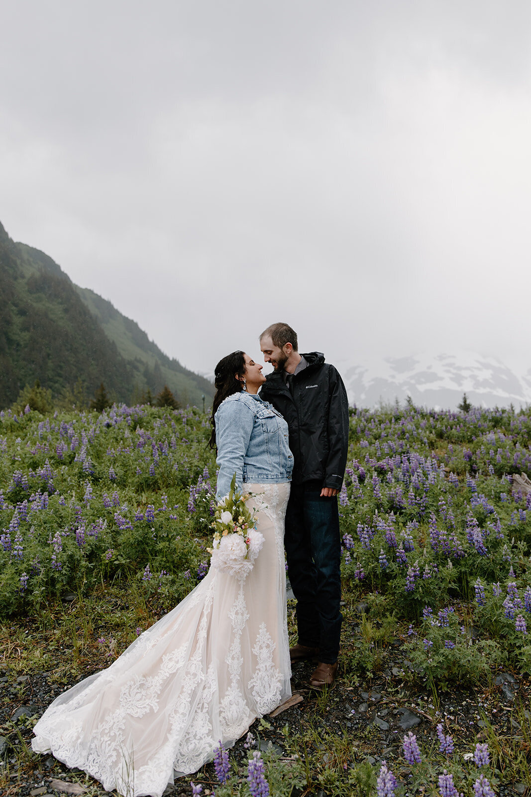 Elopement couple gazes into each other's eyes surrounded by lupine flowers.