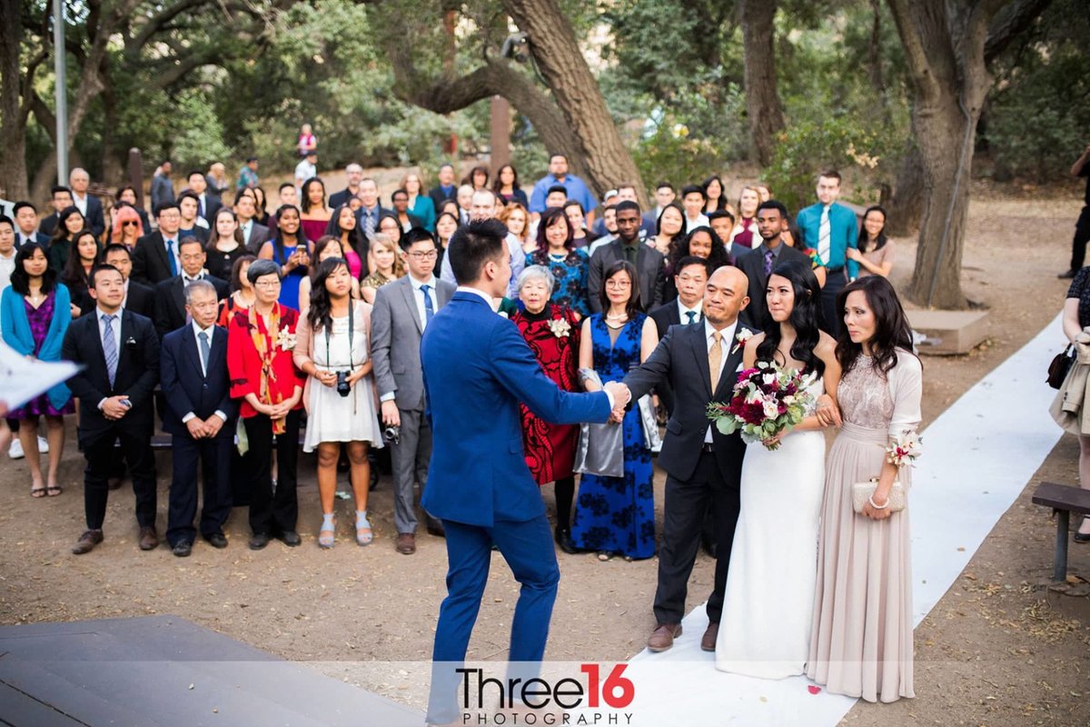 Groom shakes hand with Bride's father as her parents hand her off to him