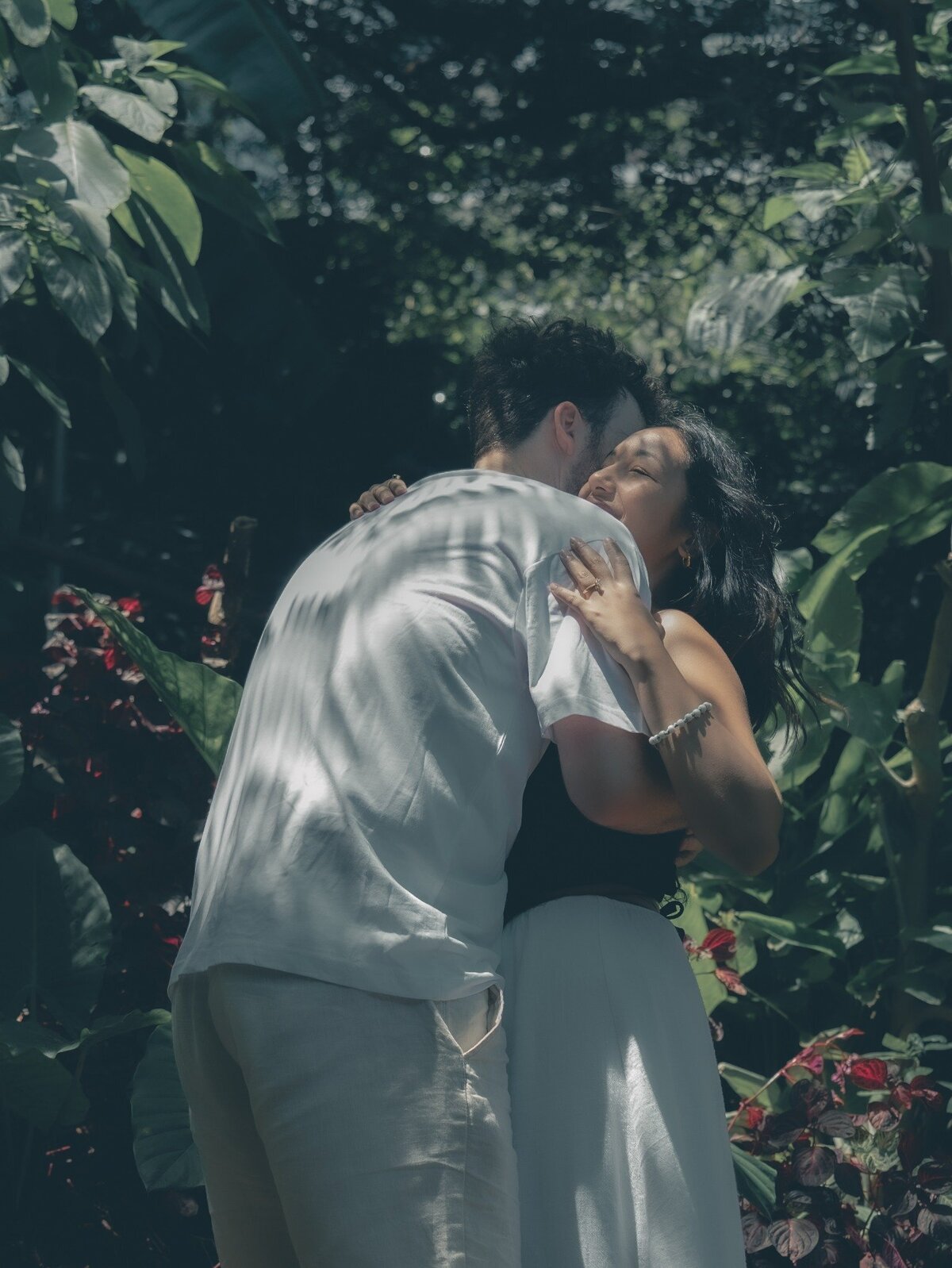 Storytelling engagement session photo of a couple hugging warmly under the trees at Wendy’s Secret Garden, Sydney.