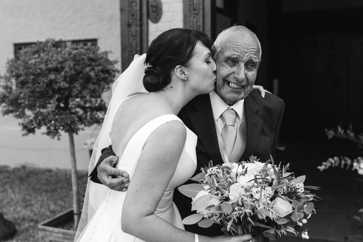 bride kisses granded during candid photography moment black and white
