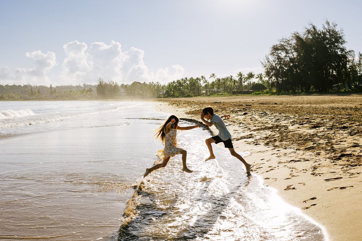 A boy and a young girl play as they jump in the water of the ocean.