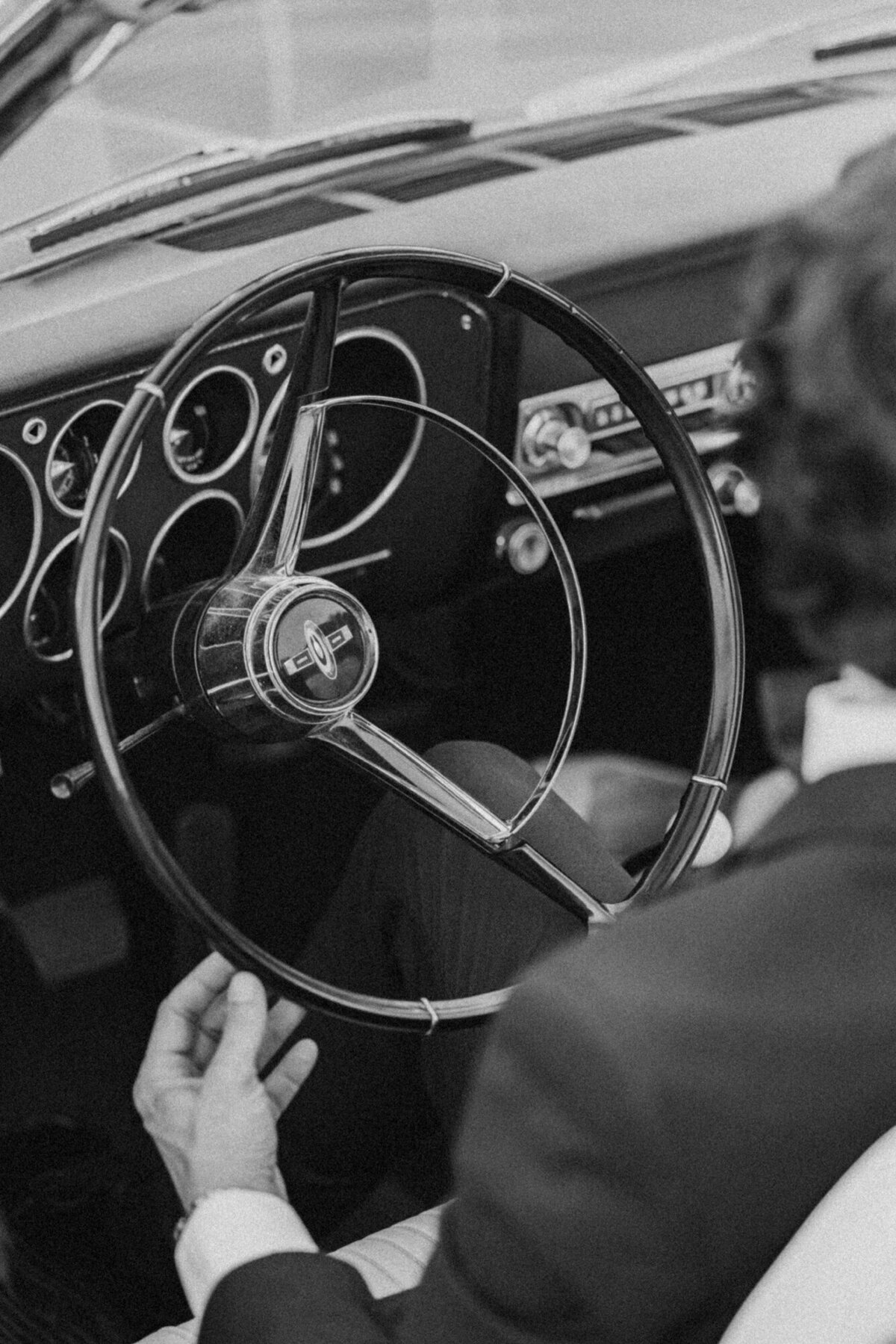 Black and white photo of couple through the windshield of a classic car, editorial style with timeless elegance.