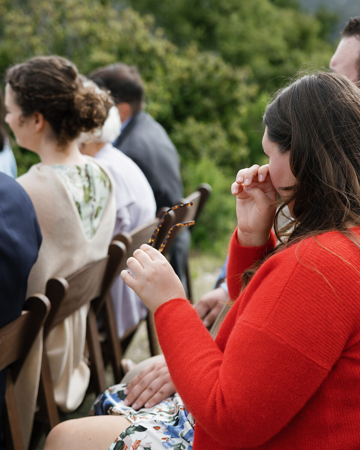 Guest in a red sweater wiping a tear while seated at the ceremony