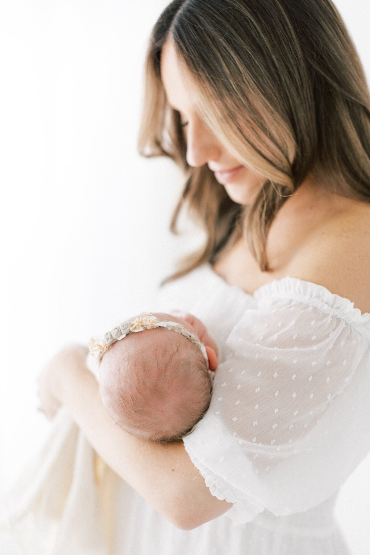 image of new mom wearing a white chiffon dress holding and looking at her week old baby captured by Dallas Newborn Photographer Amanda Carter