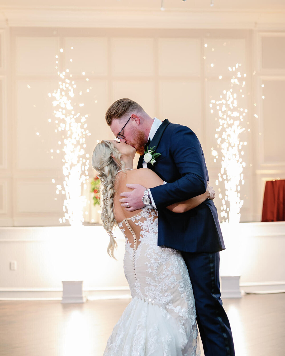 Bride and groom share a kiss during their wedding reception surrounded by indoor fireworks.
