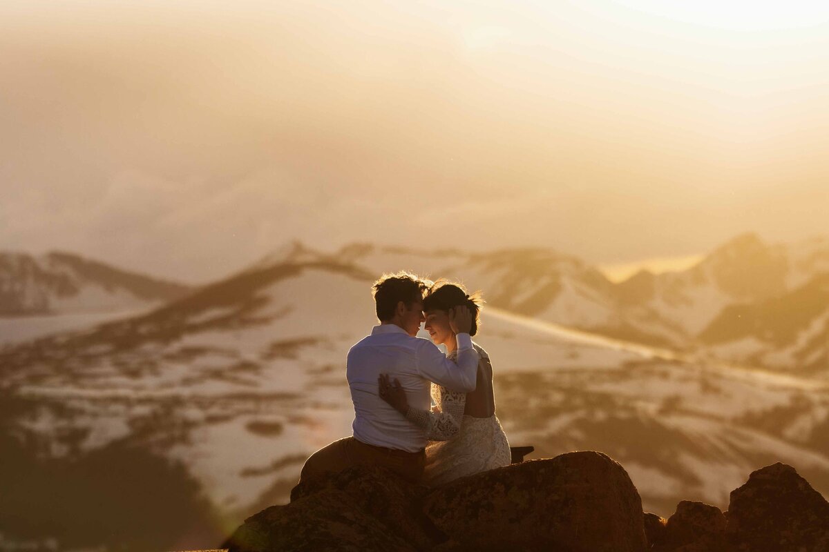 Shannon Lee, from Love Like Wild Photography, captures a couple embracing at sunset with snow-capped mountains in the background.