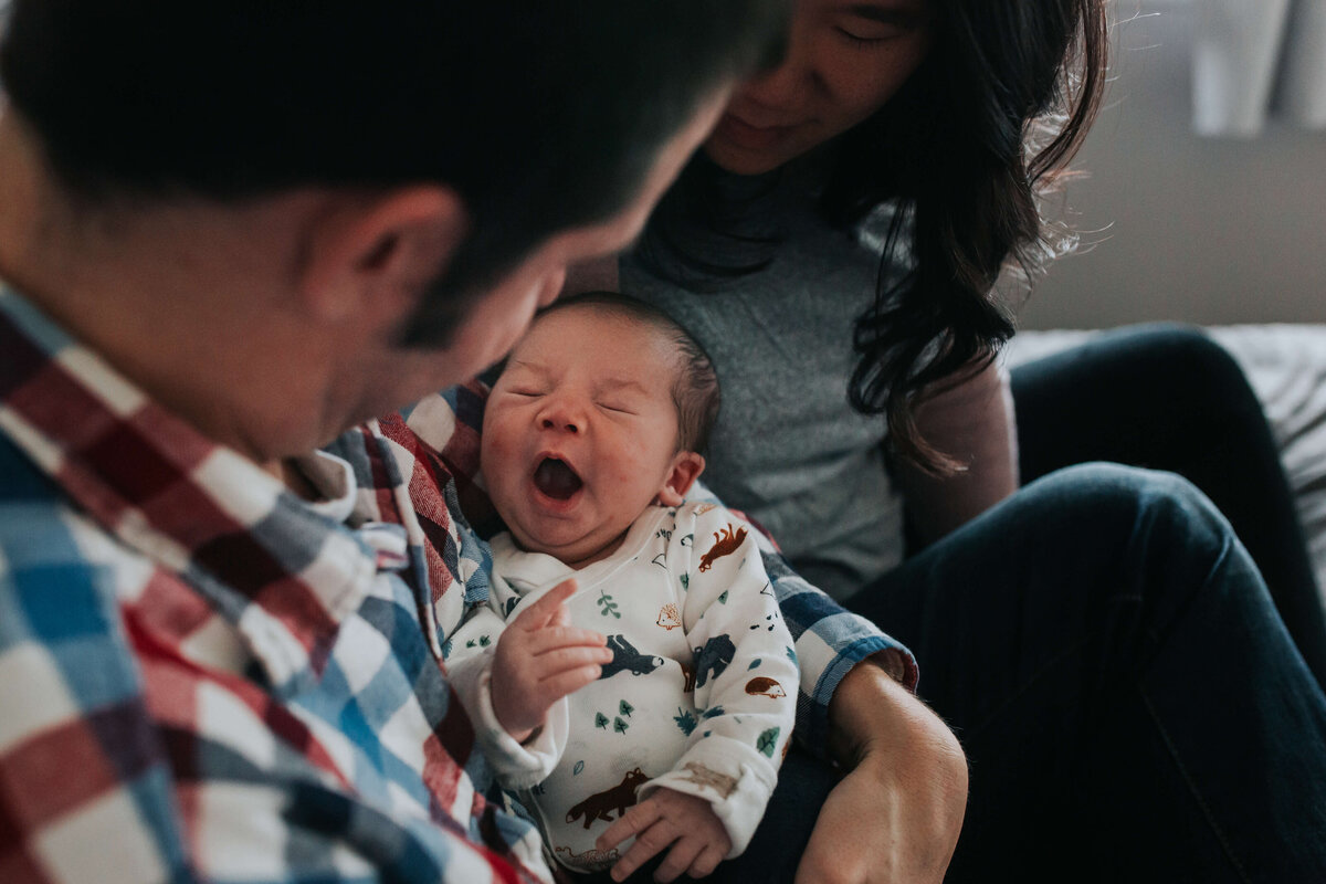 A baby boy yawning in his dad's arms while mom watches