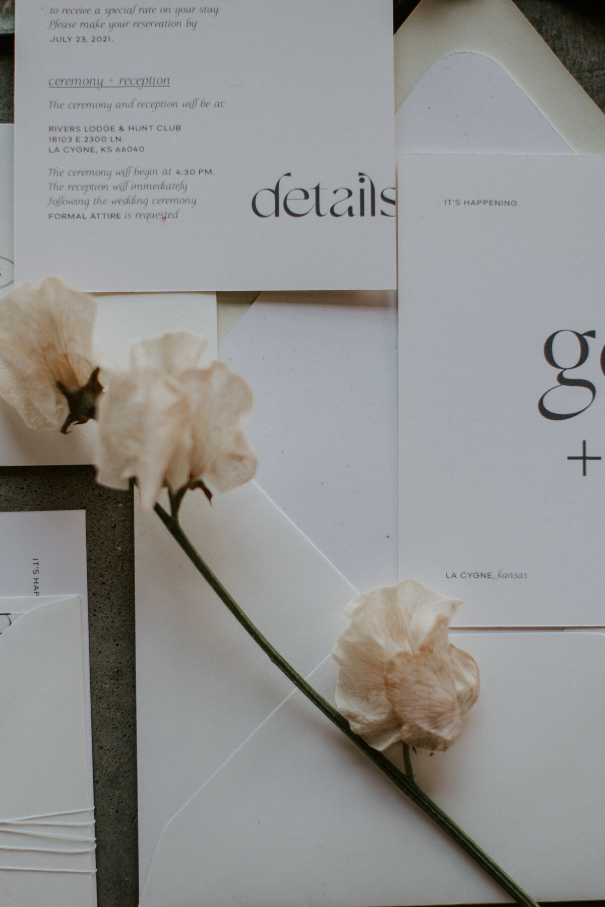 Various white wedding stationery with brown font and a blush-colored flower.