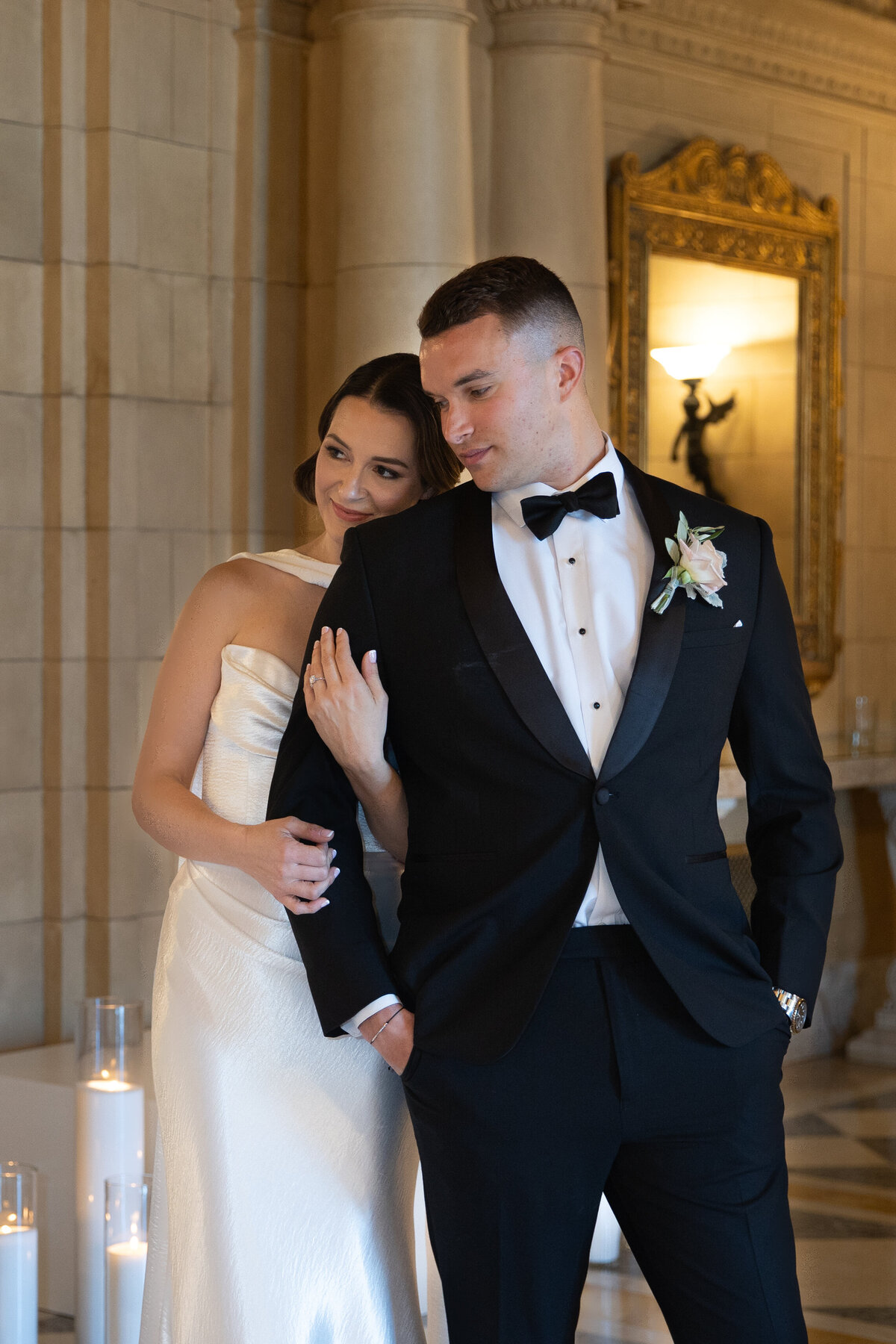 Rhode Island Wedding Photographers | Kelsey Sheehan Photography Timeless Rhode Island Weddings | A bride in a white gown and a groom in a black tuxedo stand closely in an elegant room. The bride smiles warmly, conveying love and happiness.