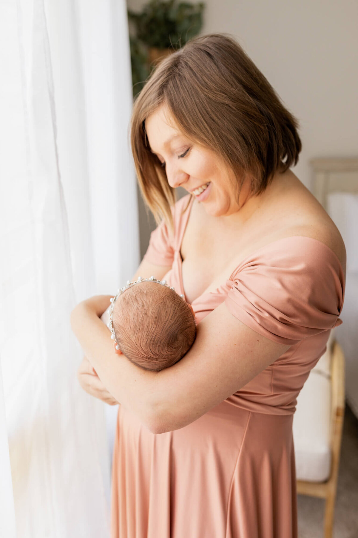 Mom in a peach dress cradling and smiling down on her newborn baby girl