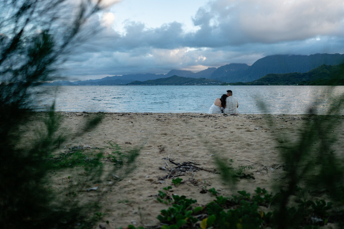 Oahu Hawaii Elopement Adventurous Asian couple at Secret Island Beach during golden sunset with mountains and ocean waves sitting.