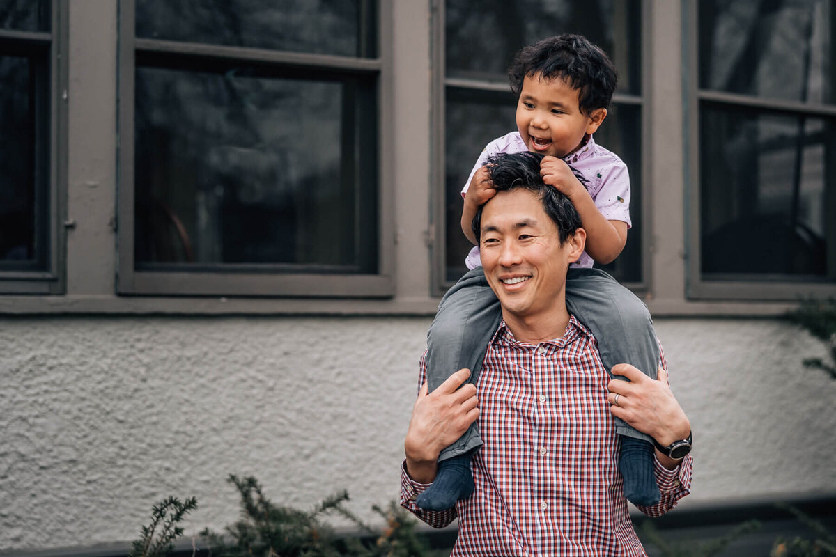 A young boy smiles and grasps his father's hair while he sits on his shoulders during an at home photography shoot.
