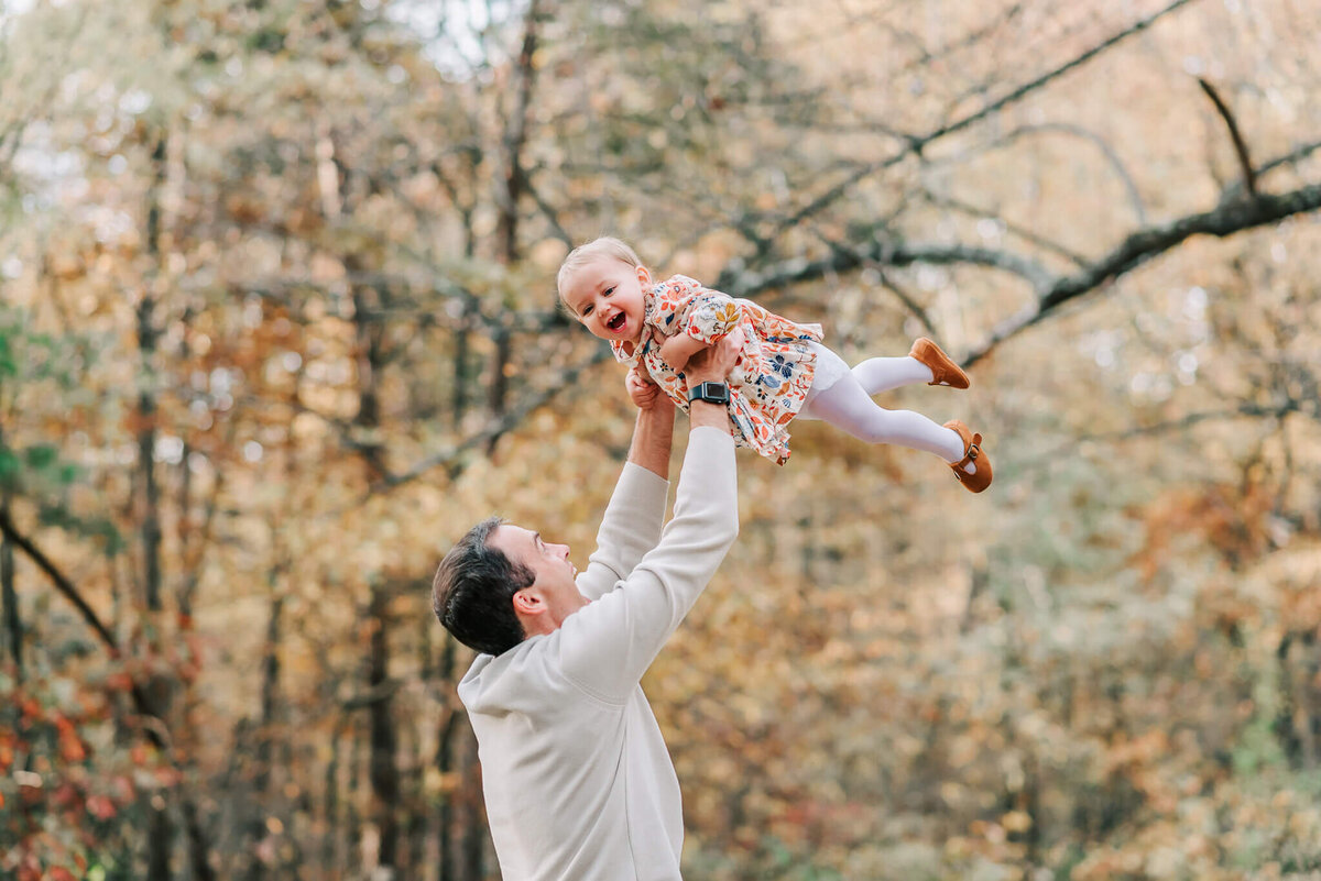 A dad lifting his child up into the air in the woods of Lake Fairfax Park
