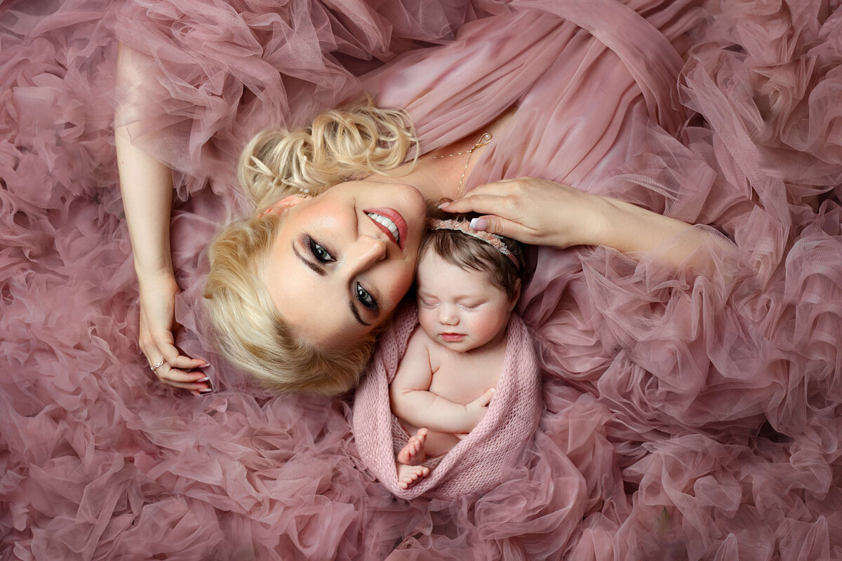 Newborn baby in a pink  wrap laying with her mom in a pink  tulle dress in a northern virginia  newborn photo studio