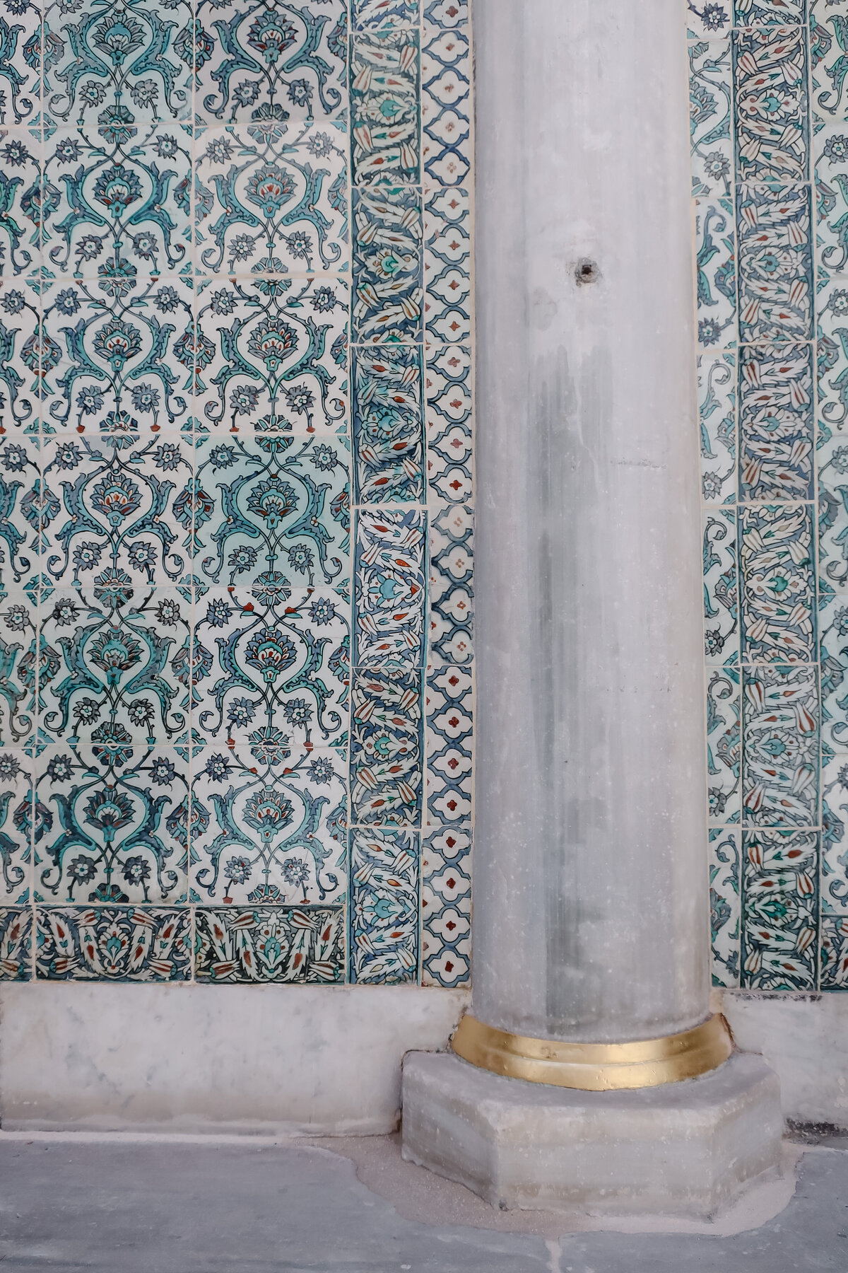Turkish tiles in blue, gree, red, and white showing interwoven flowers sits behind a column with gilded base