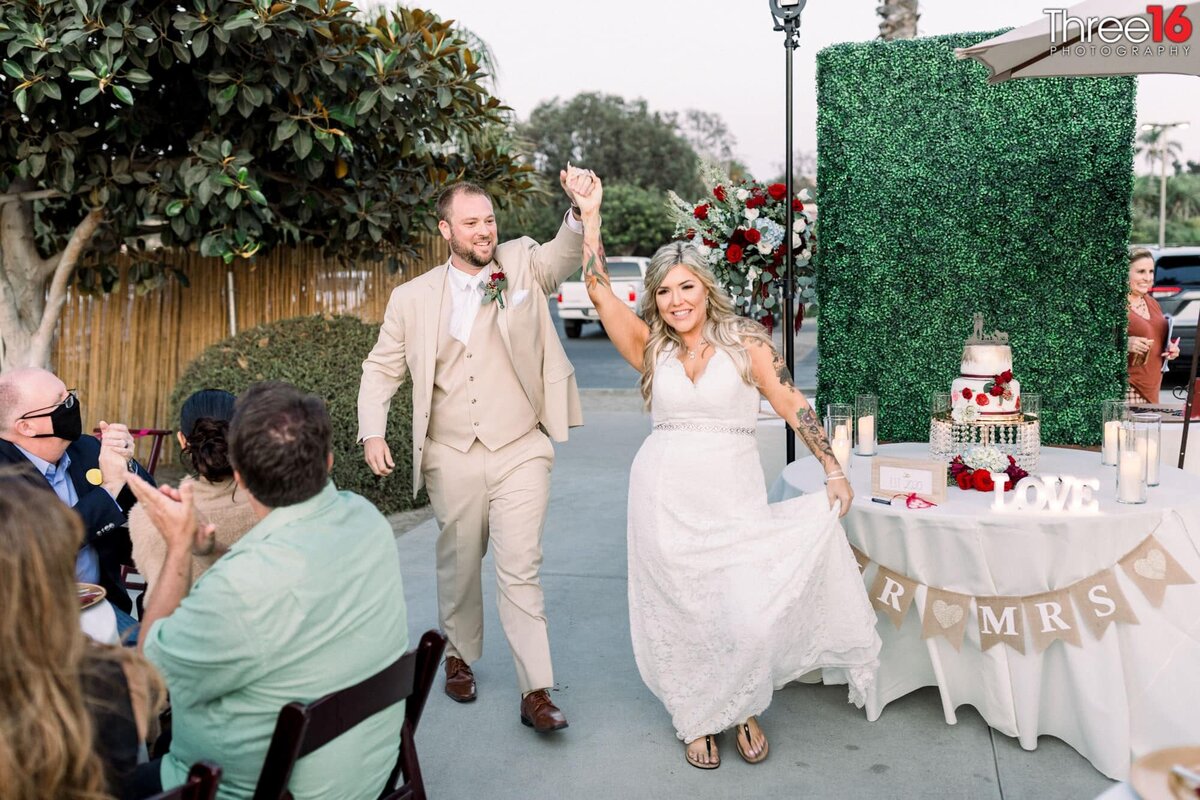 Bride and Groom celebrate with their held hands in the air as they are introduced to the wedding reception