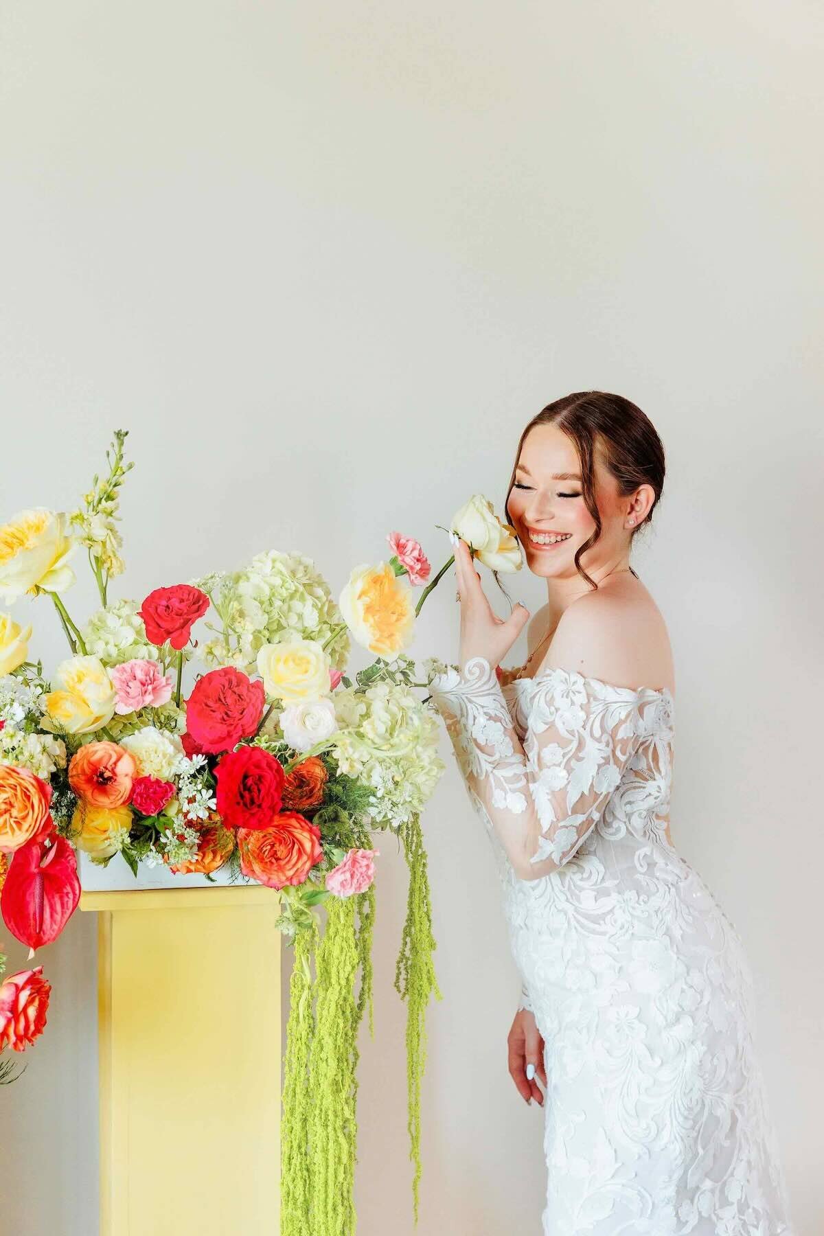 Bride posing with colorful florals in a strapless gown, smiling beside a vibrant wedding arrangement.